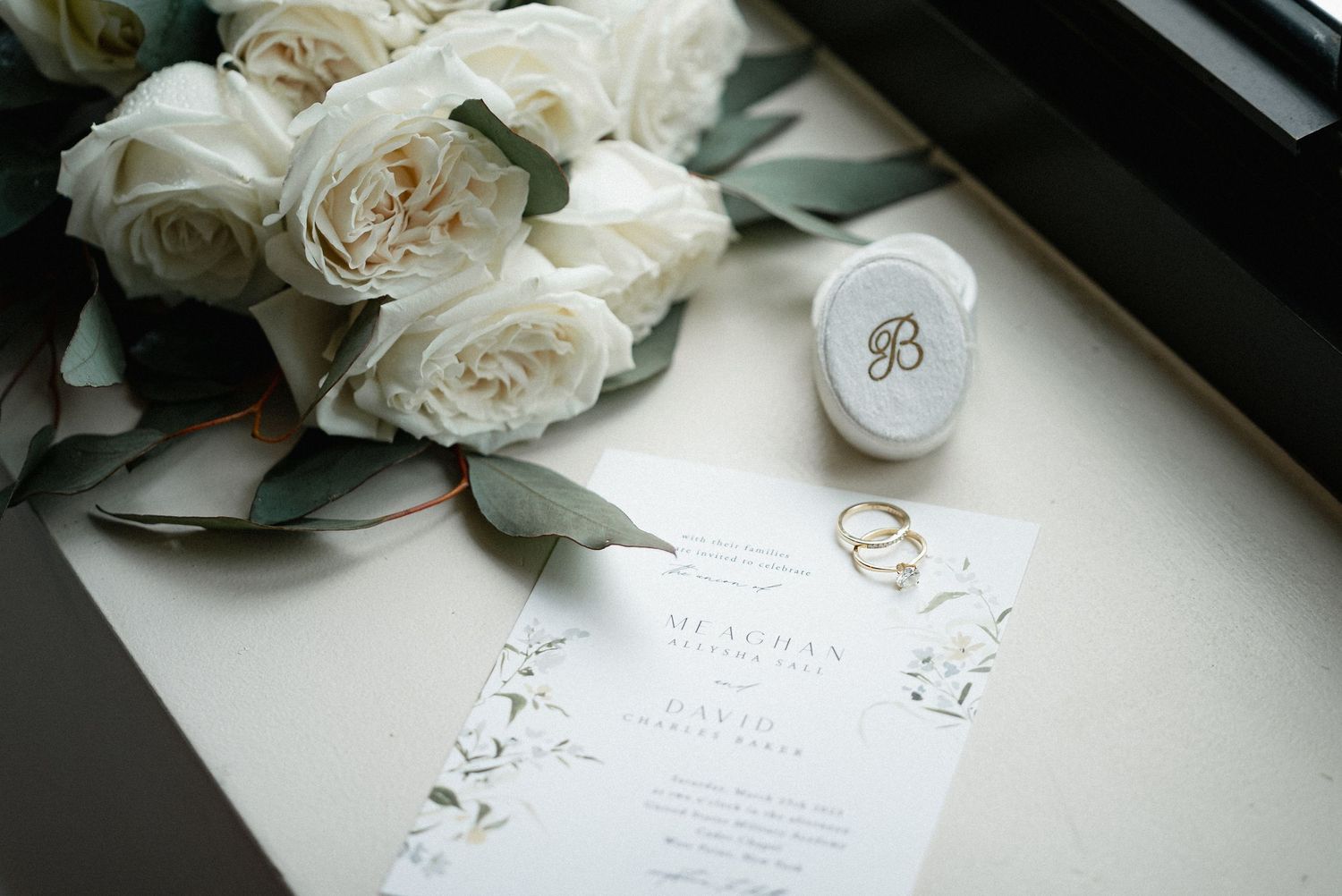 White roses and wedding stationery arranged on a light surface.