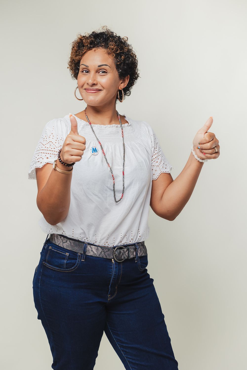 Person in white eyelet top giving thumbs up against white background.