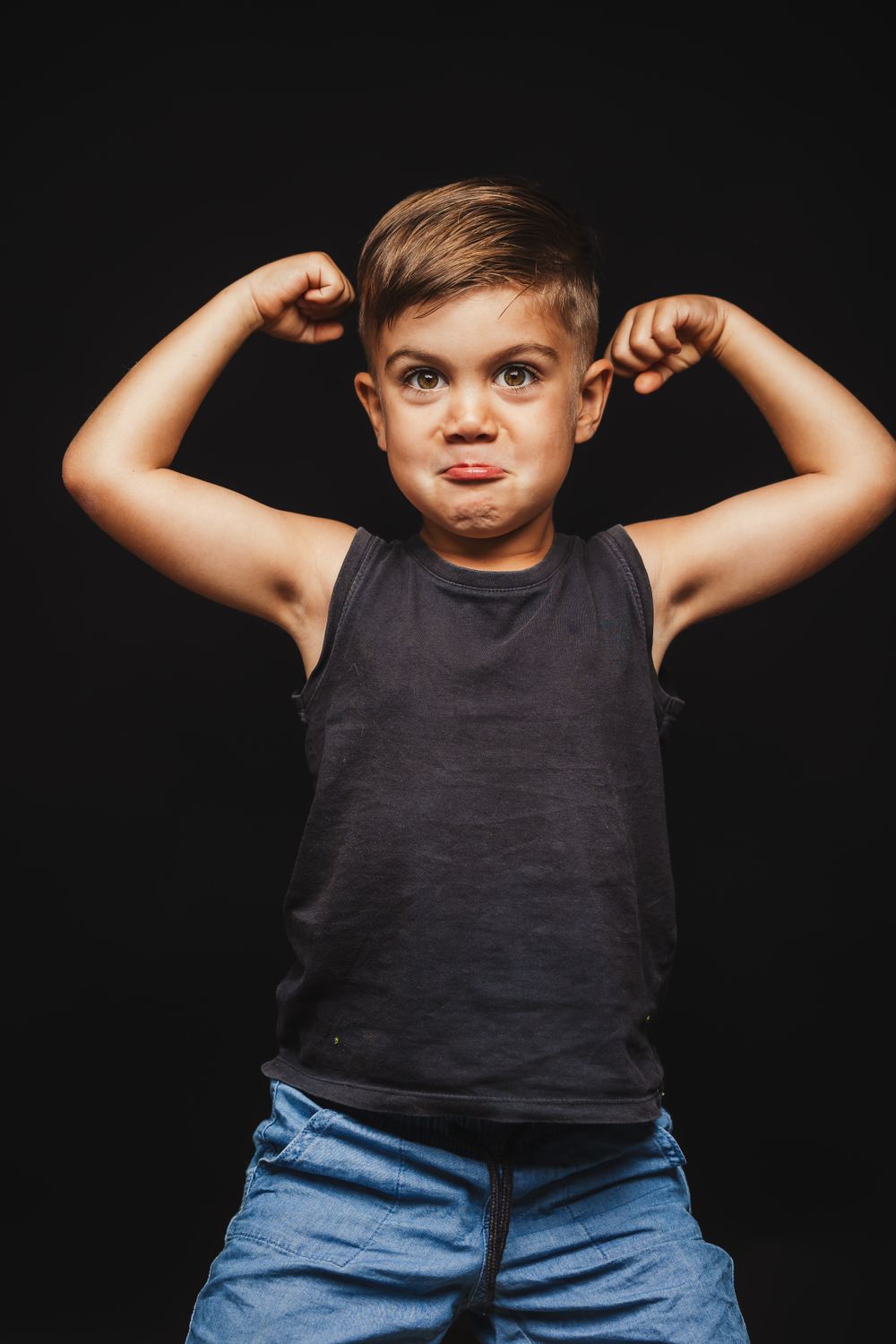 Sequence showing a child in black tank top flexing muscles against dark background.