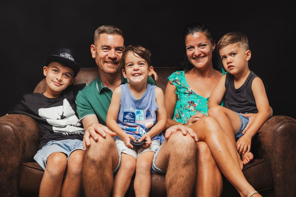 Family group relaxing together on brown leather couch in casual attire.