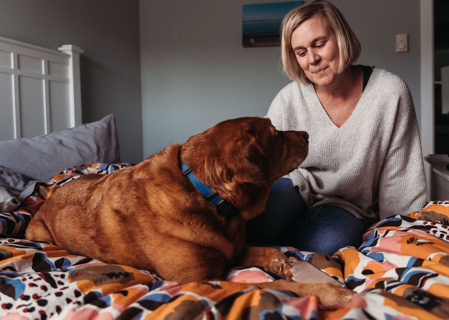 Woman relaxing on a bed with her large brown dog wearing a blue collar.