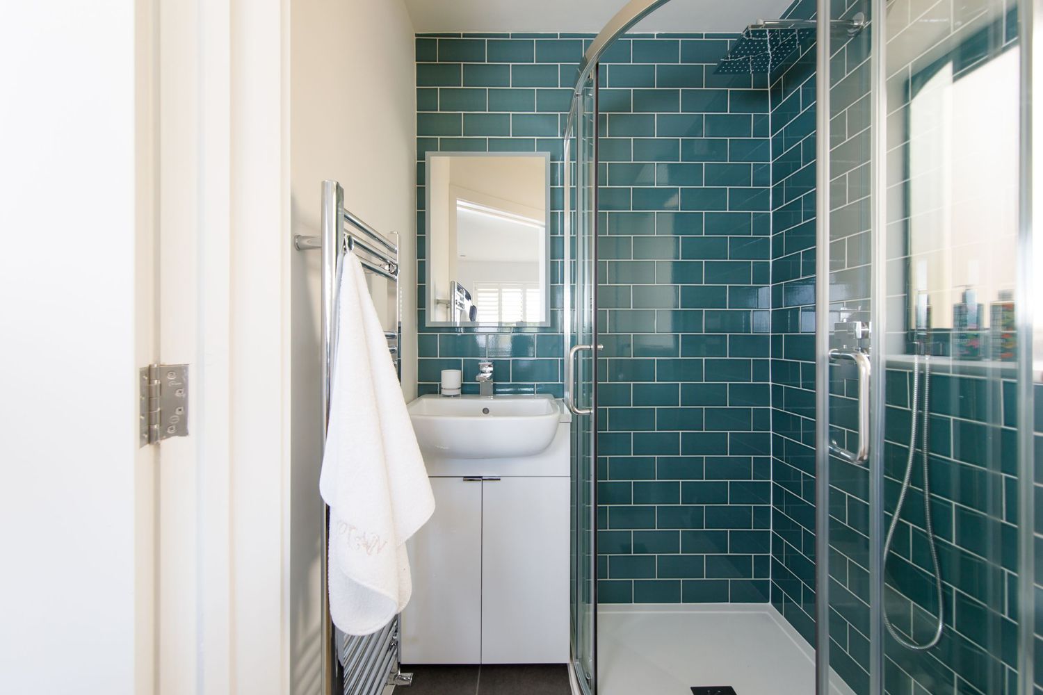 Modern bathroom featuring turquoise subway tiles and glass shower enclosure.