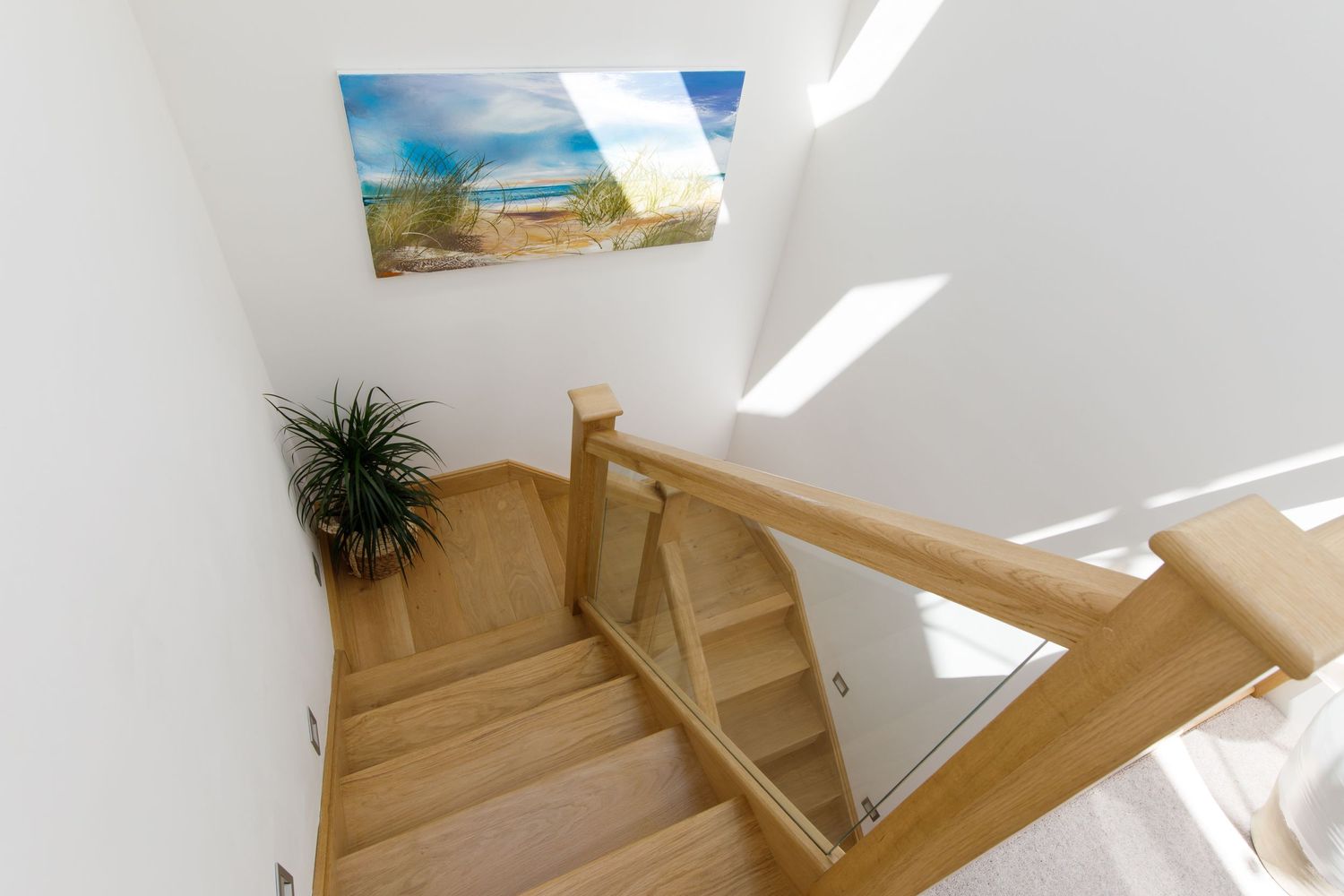 Wooden staircase with skylight and coastal artwork on white walls.