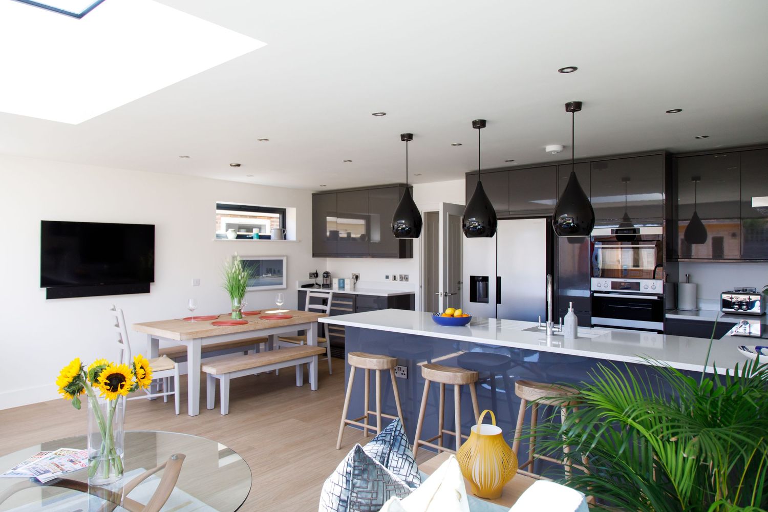 Contemporary open plan kitchen and dining area with black pendant lights and wooden furniture.