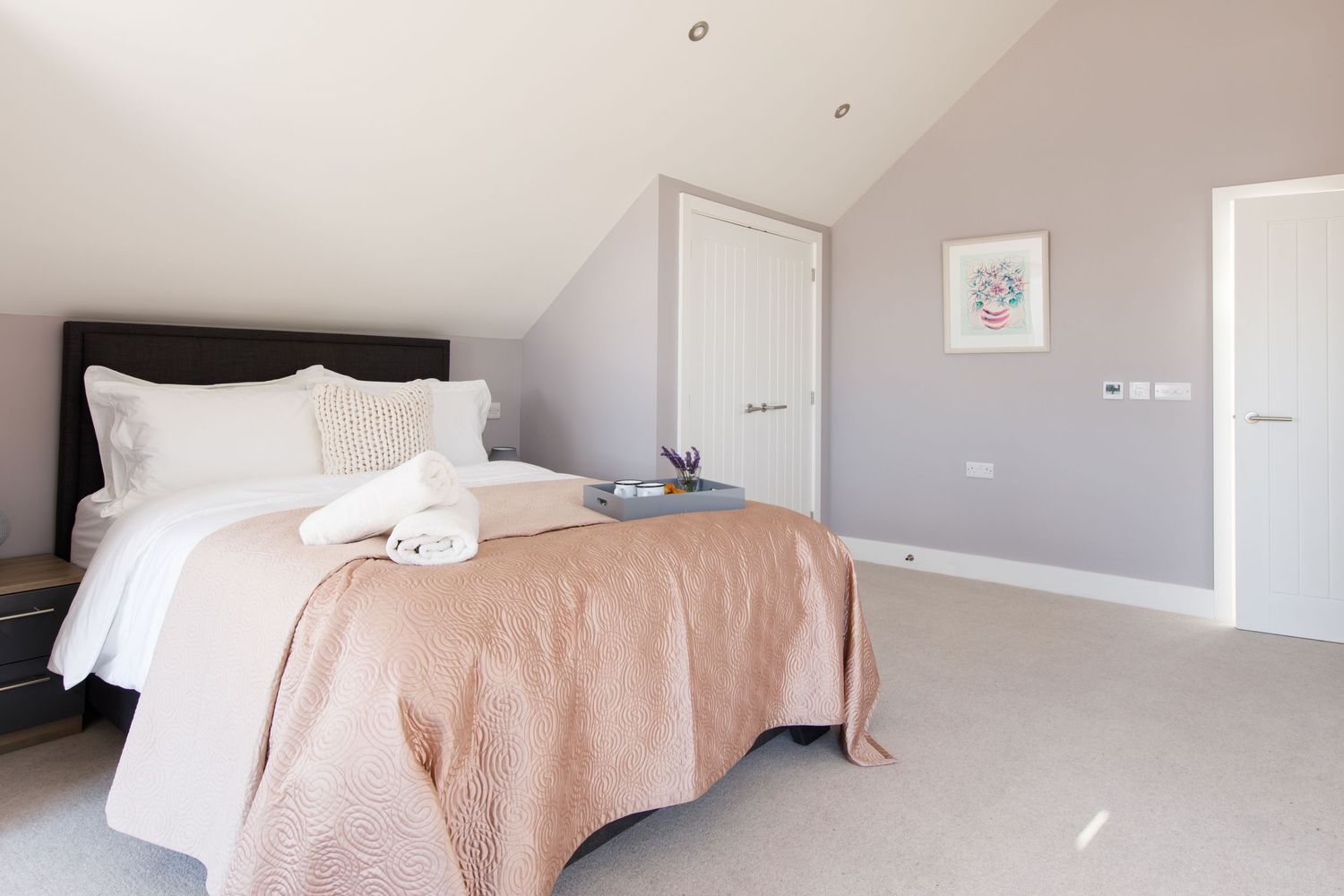 Minimalist bedroom with pink bedding and sloped ceiling in neutral tones.