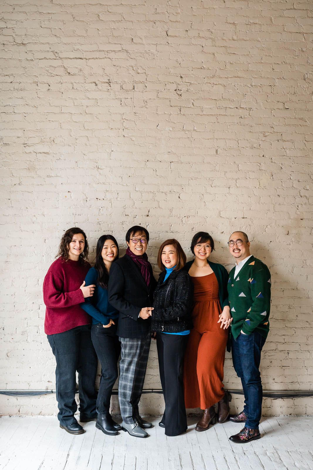 Extended family poses for indoor family photos against a brick wall.