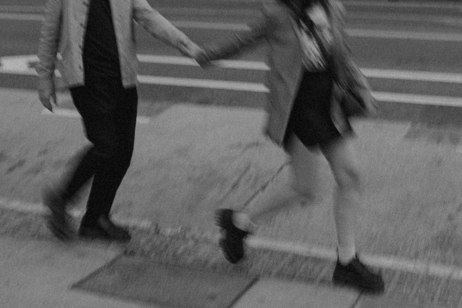 Grainy, black & white photograph of couple running together while holding hands. Motion blur, cropped below their chest.