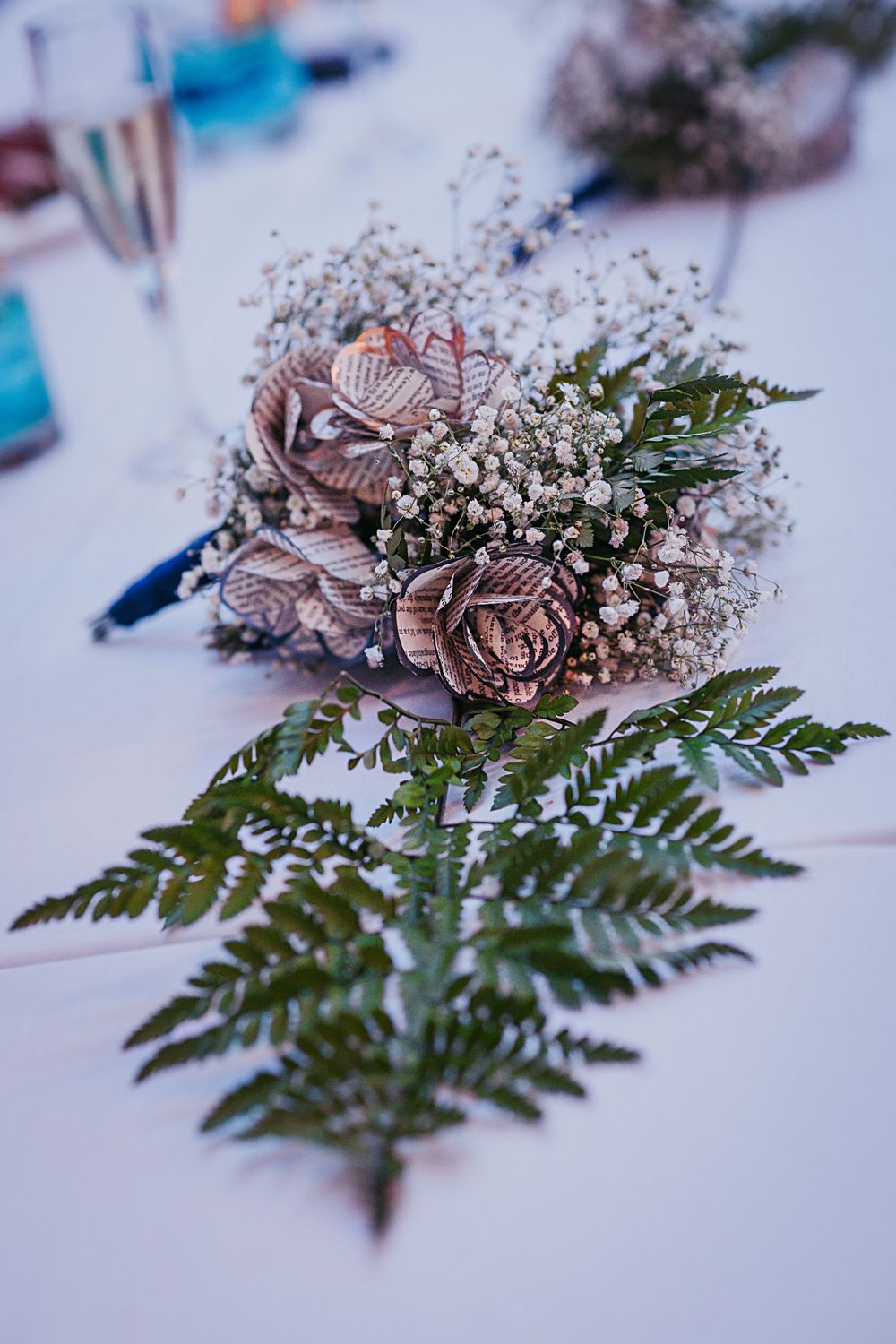 Vintage-style paper roses and baby's breath floral arrangement with ferns on a white tablecloth.