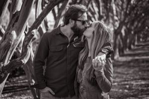 A romantic couple shares a tender moment in a tree-lined path.