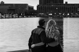 An engaged couple watching the sunset together by waterfront with Baltimore cityscape in the background.