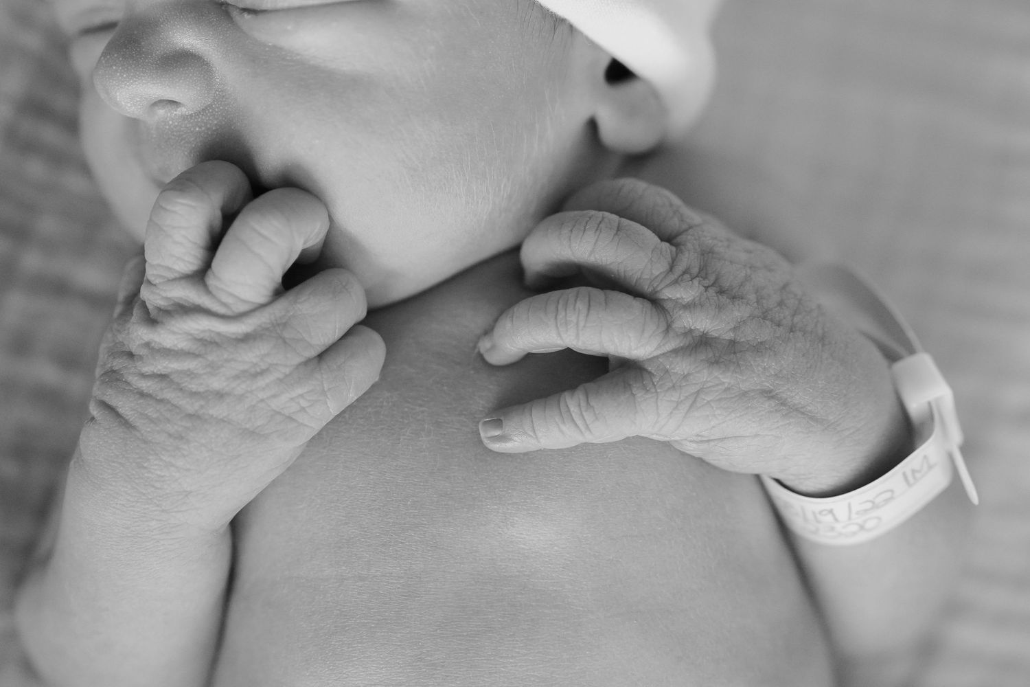 Close-up black and white photo of elderly hands gently holding a baby's face.