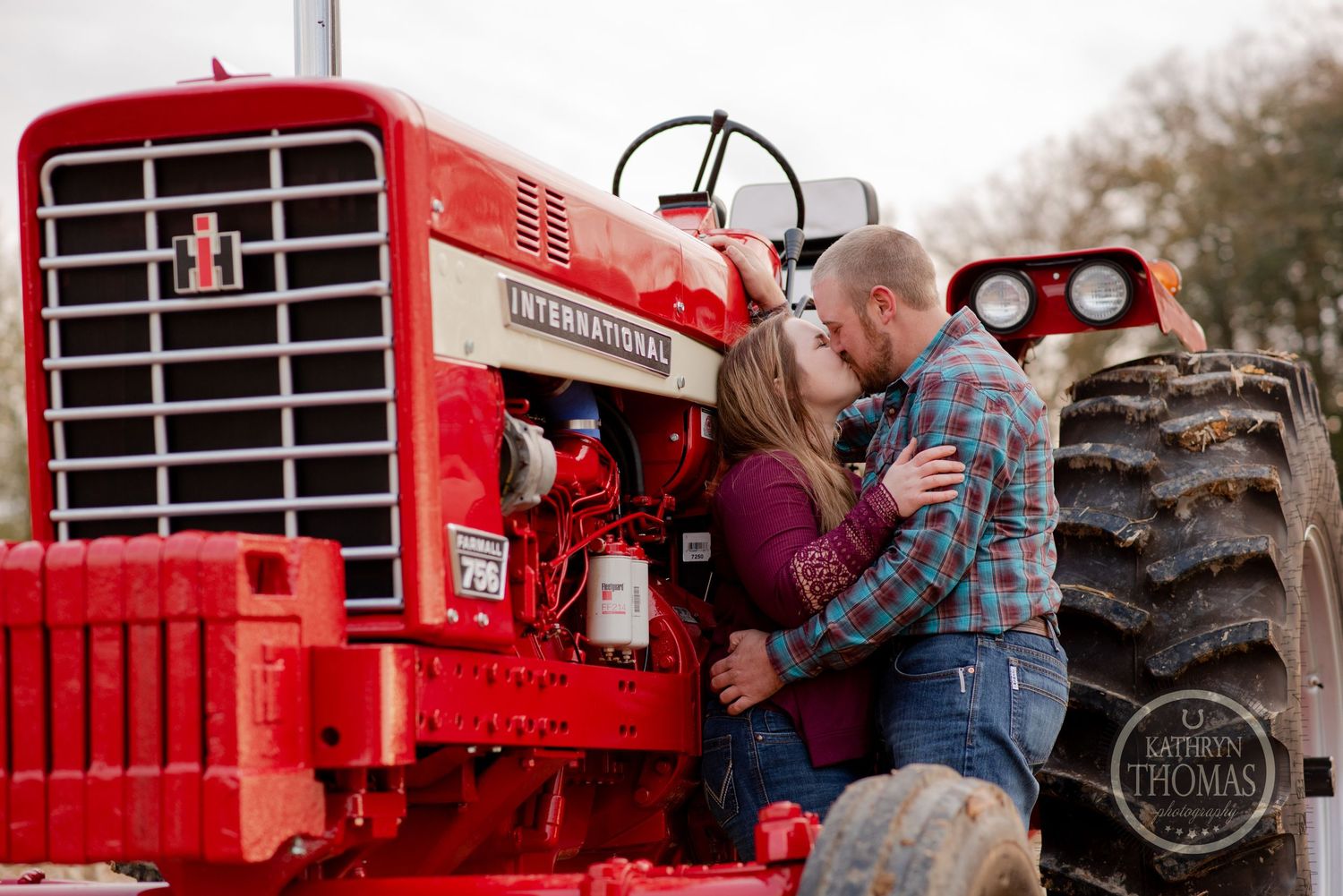 A couple embracing against a bright red vintage International tractor in a rural setting.