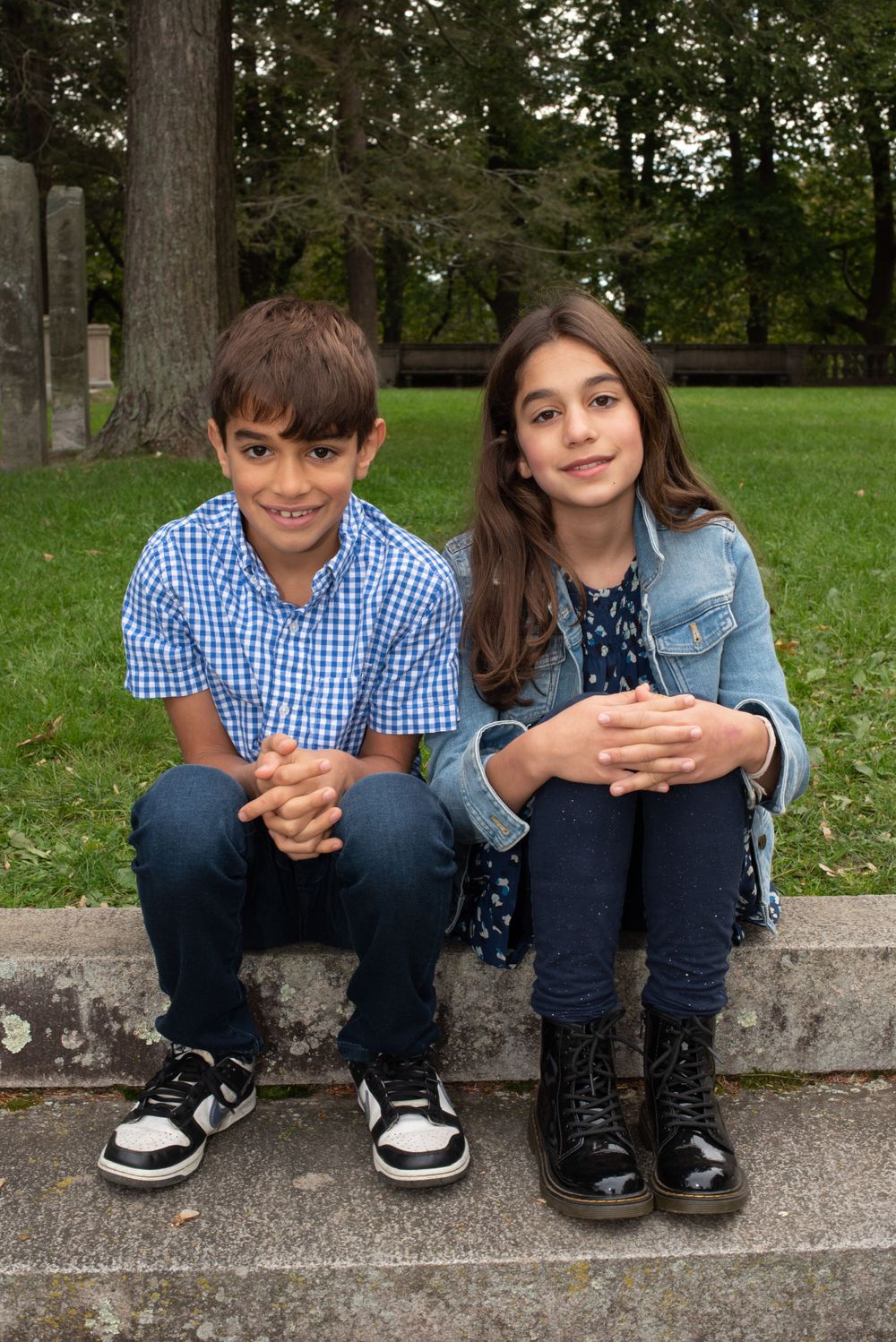 Two children sitting side by side on a stone ledge in an outdoor park setting.