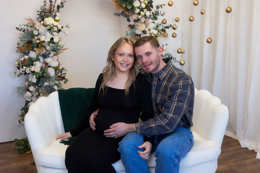 Holiday maternity photo with couple on white couch with floral arch.