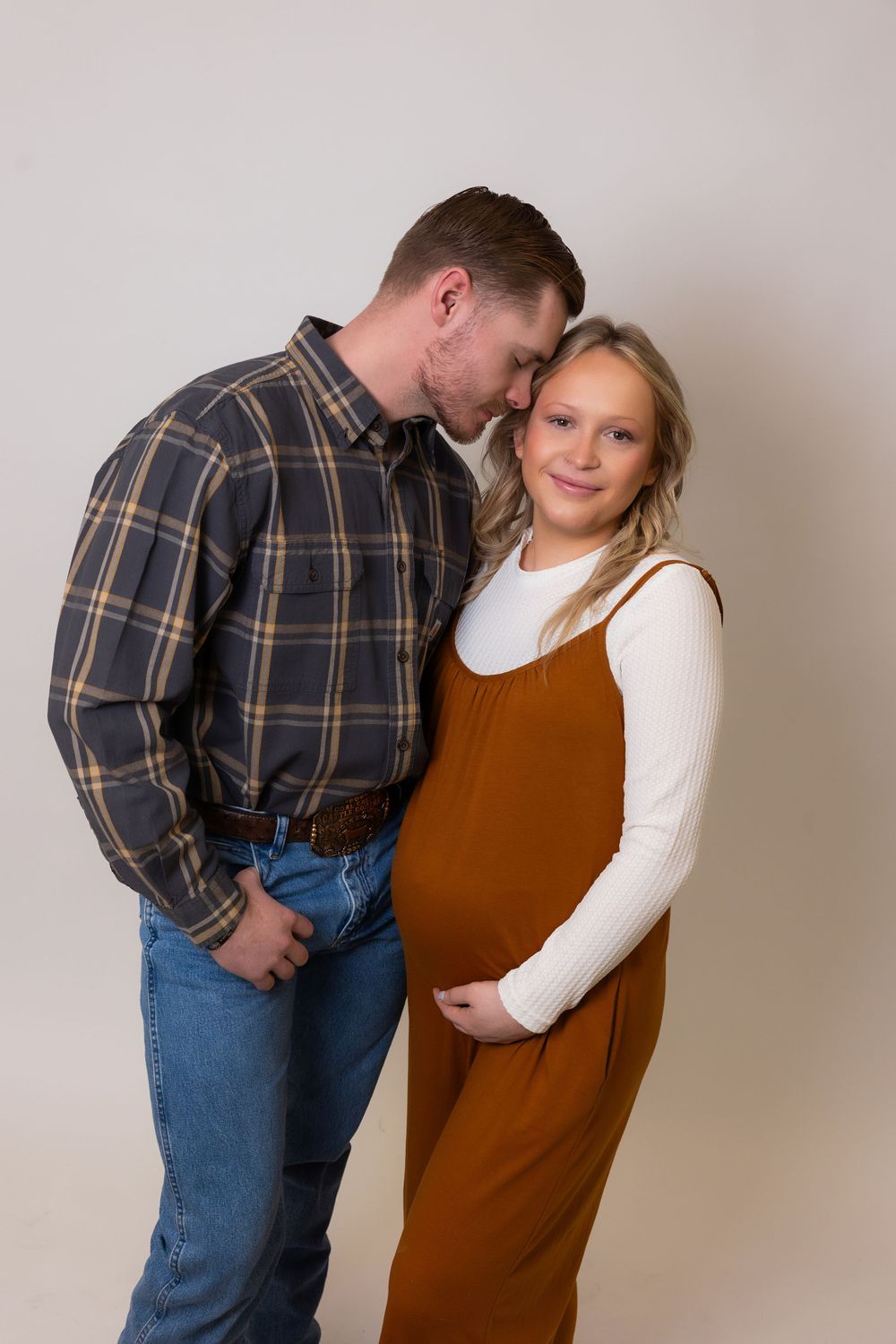 Maternity photoshoot features couple in plaid shirt and rust-colored overalls.