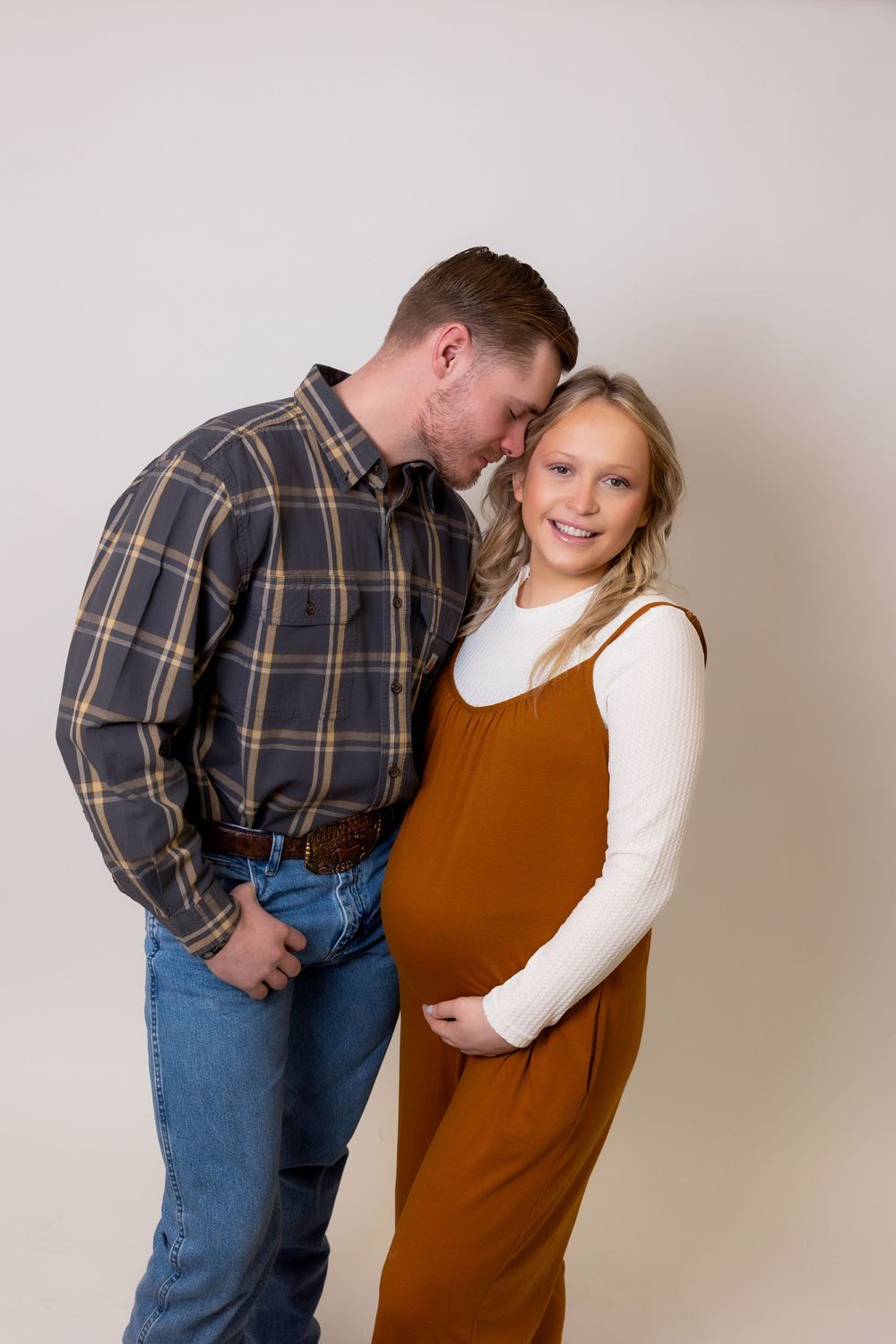 Expecting couple shares tender moment in casual attire during photo session.