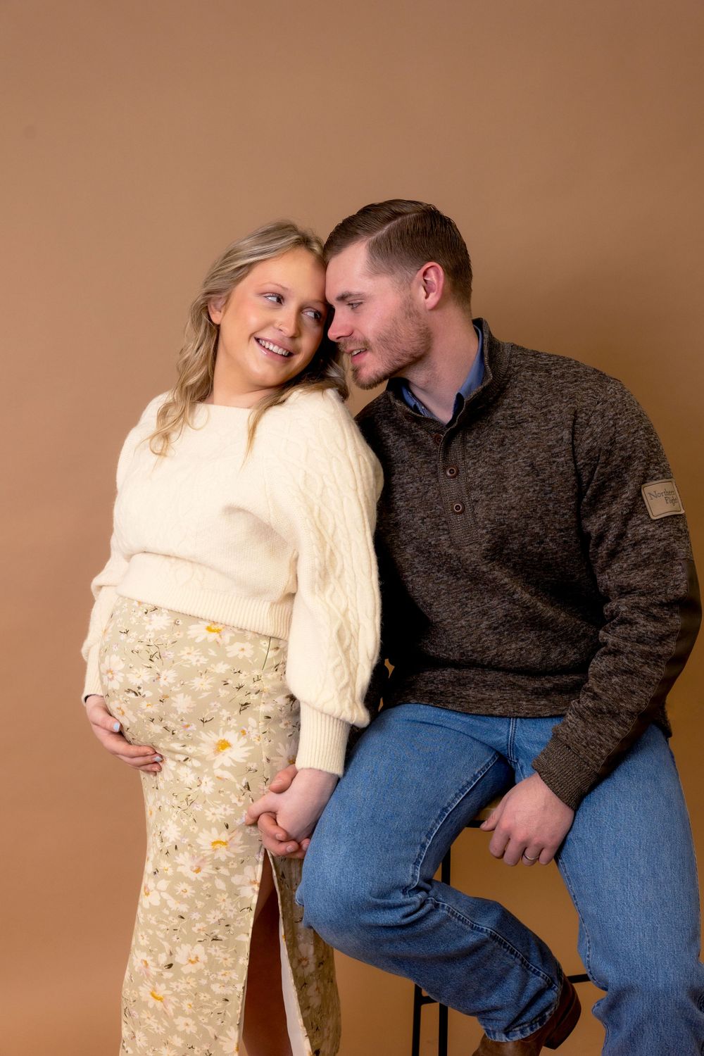 A tender moment captured during a maternity photoshoot with a couple in warm winter clothing.