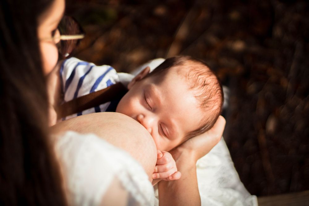 Mother holding baby close during a quiet nursing moment, surrounded by nature.