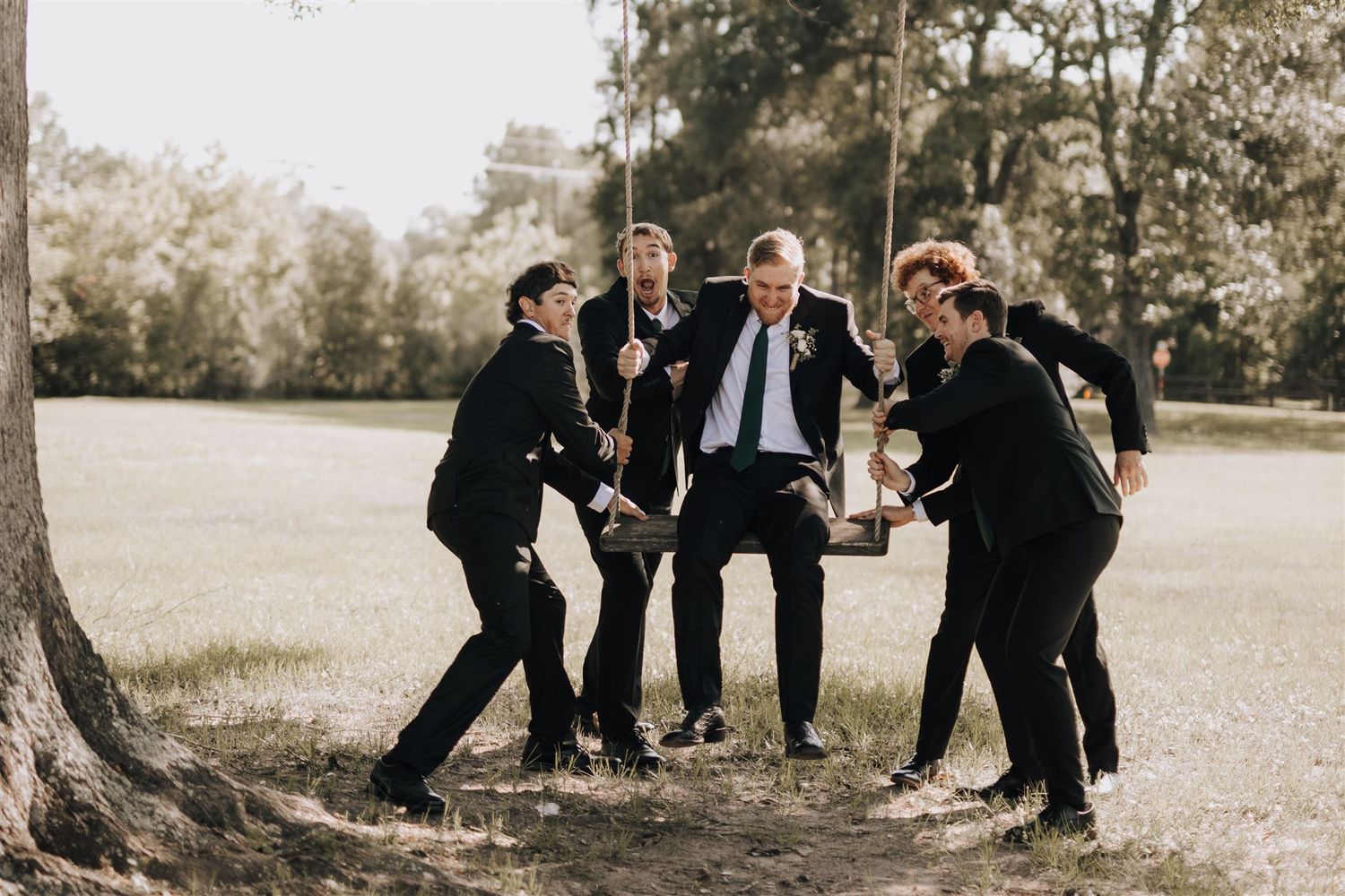 Groomsmen laughing and having fun together outdoors in formal black suits.