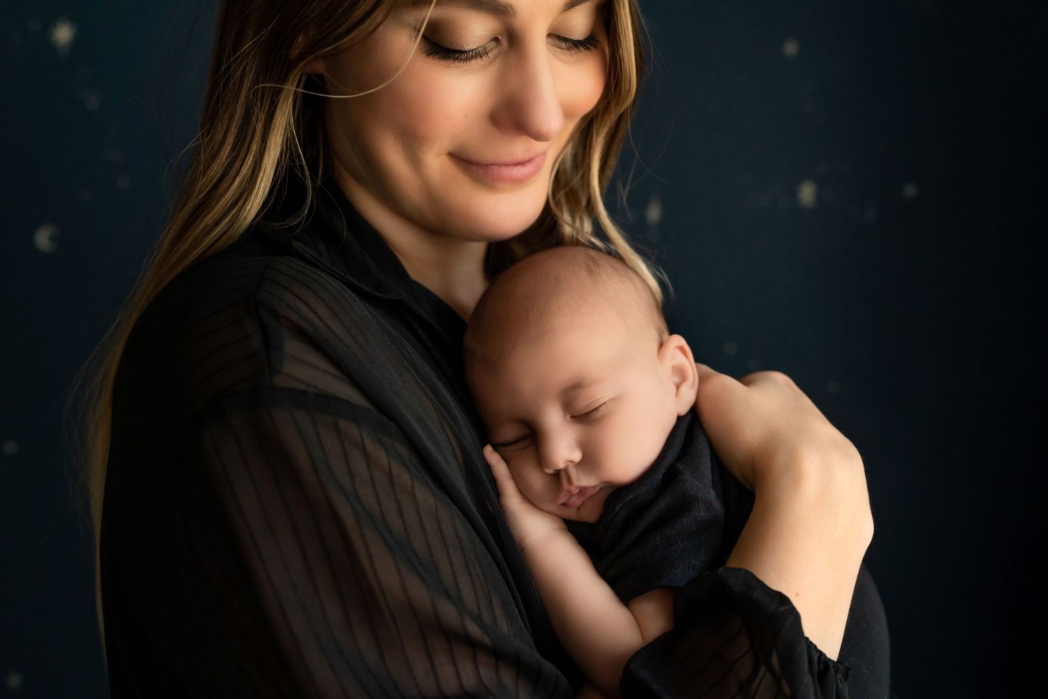 Tender moment between mother and sleeping baby against dark starry background.