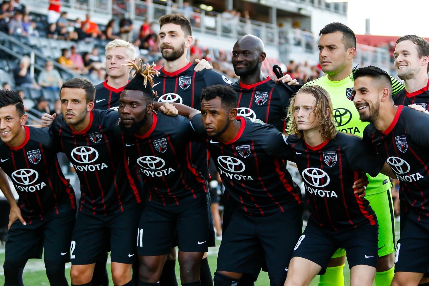 Soccer team lined up on field wearing black uniforms with Toyota sponsorship.