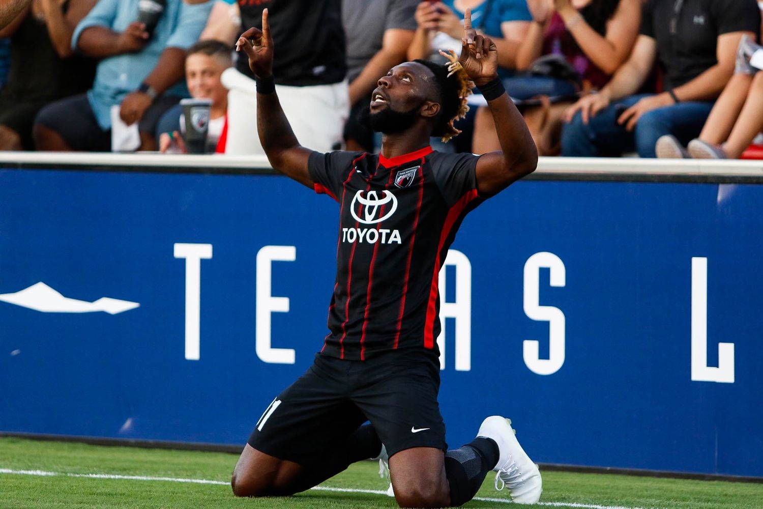 Soccer players celebrating a goal during a match on a blue-tinted field.