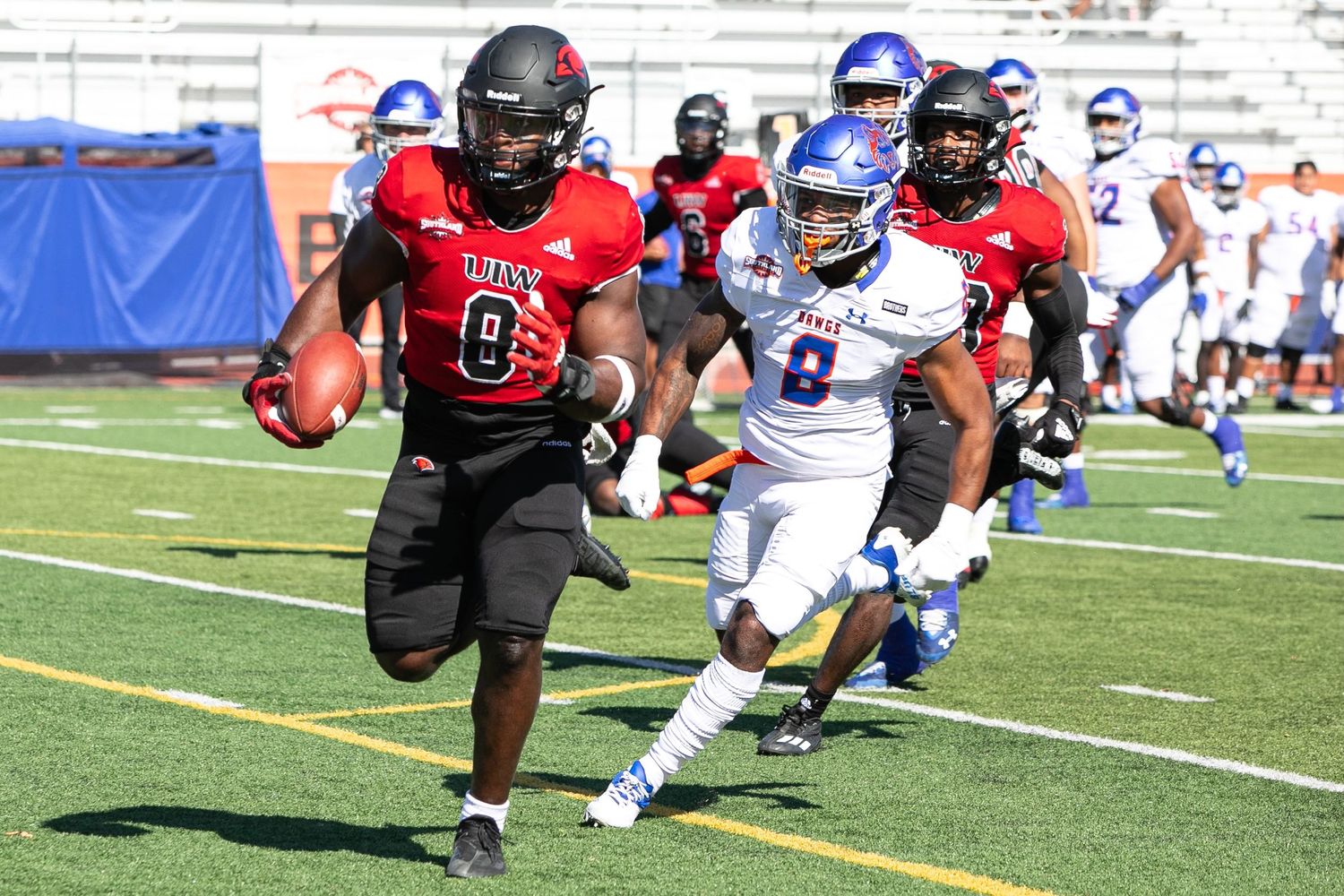 Football players in red and white uniforms competing on a sunny field.
