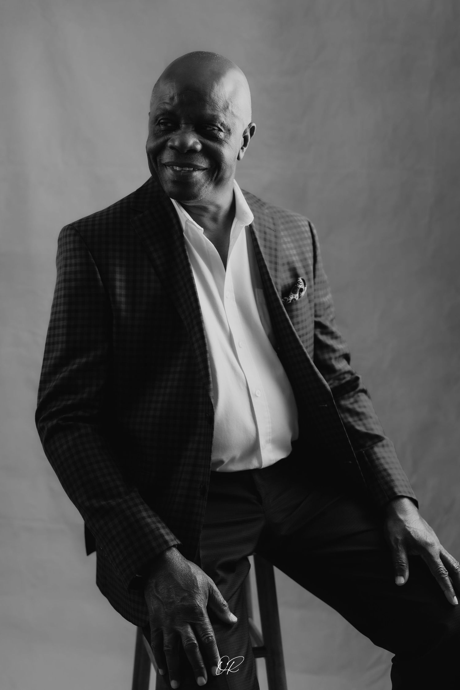 A black and white portrait shows a sophisticated pose in a tailored blazer and dress shirt.