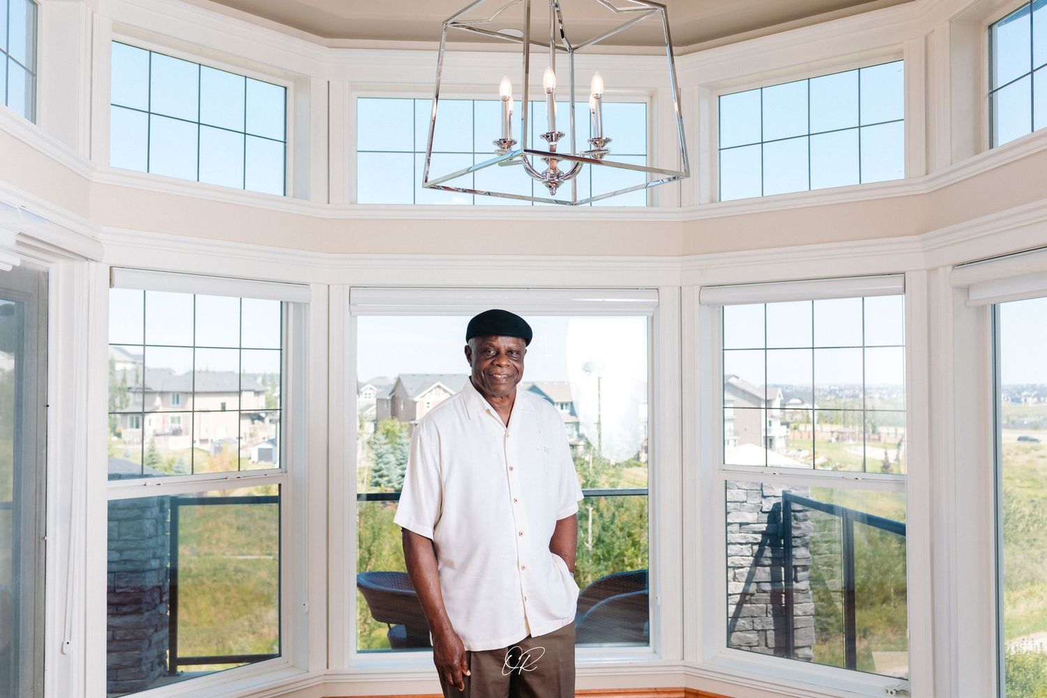 An elegant sunlit room features white bay windows and a modern chandelier.