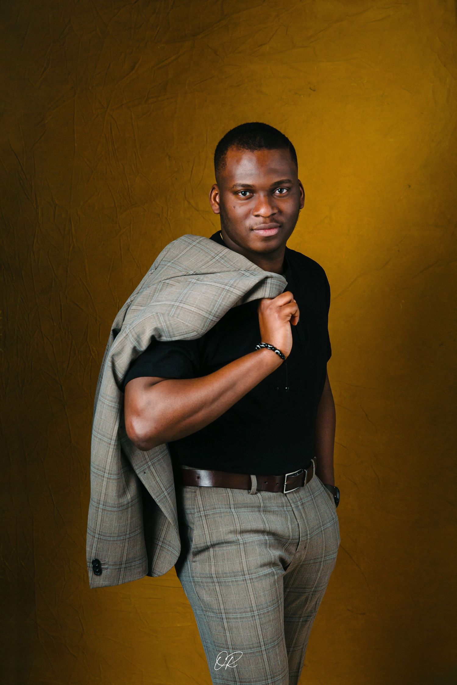 Professional portrait with person holding grey suit jacket against golden background.
