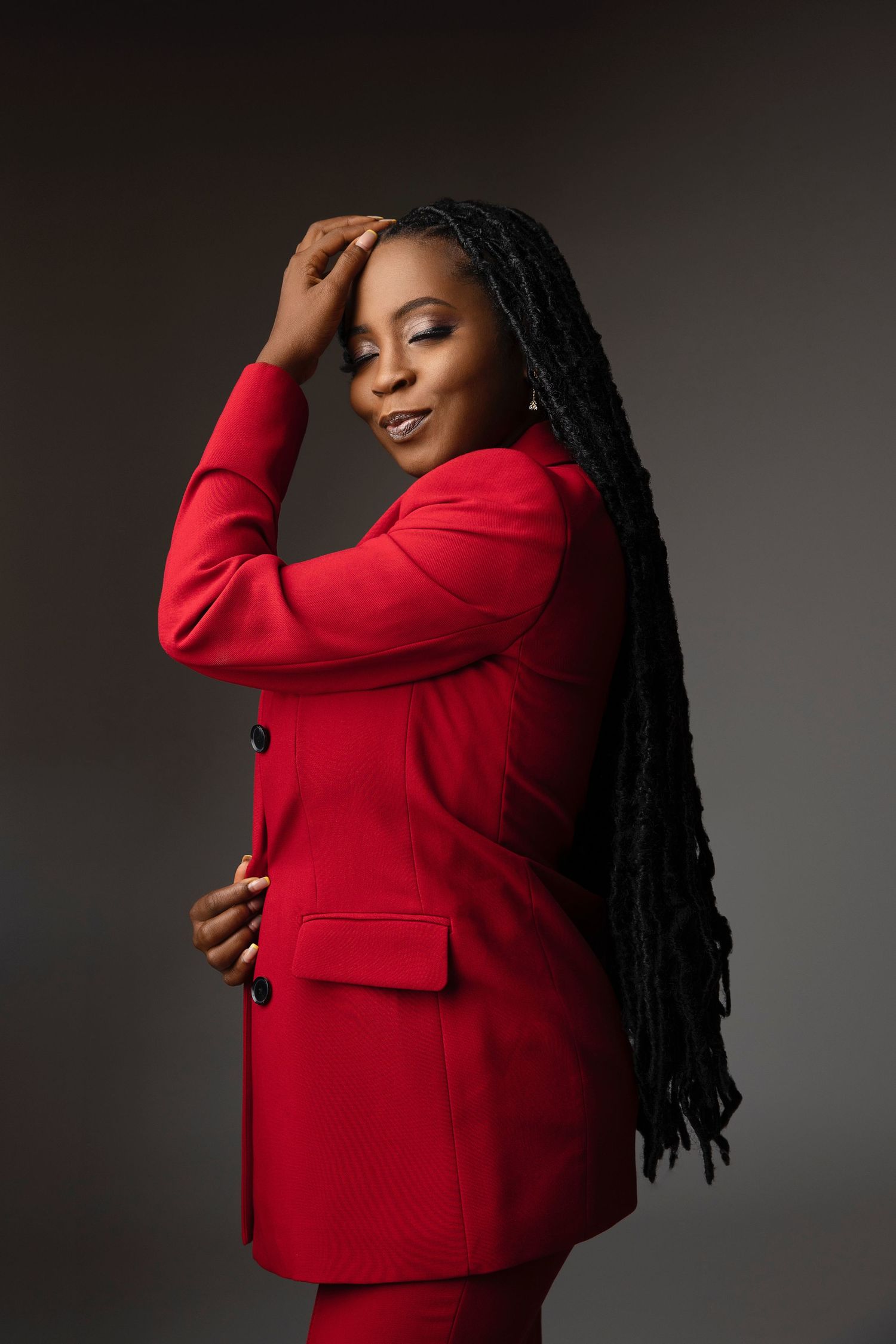 A model in a vibrant red blazer poses gracefully against a dark background.