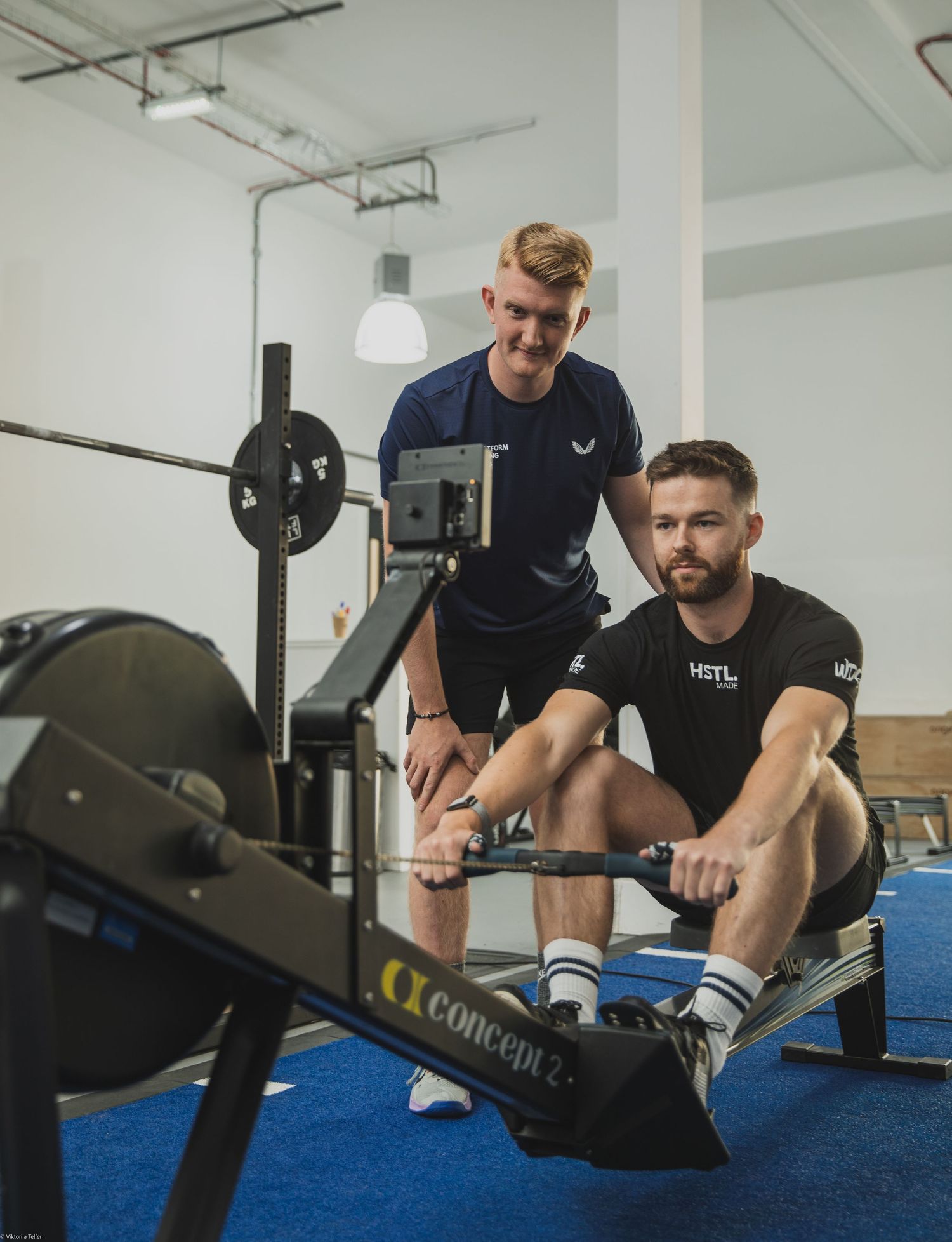 Athletes training with rowing machines on blue gym floor.