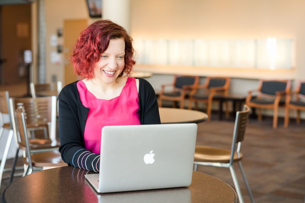 A woman wearing a pink shirt works on her computer in her office building. Maple Ridge, BC.