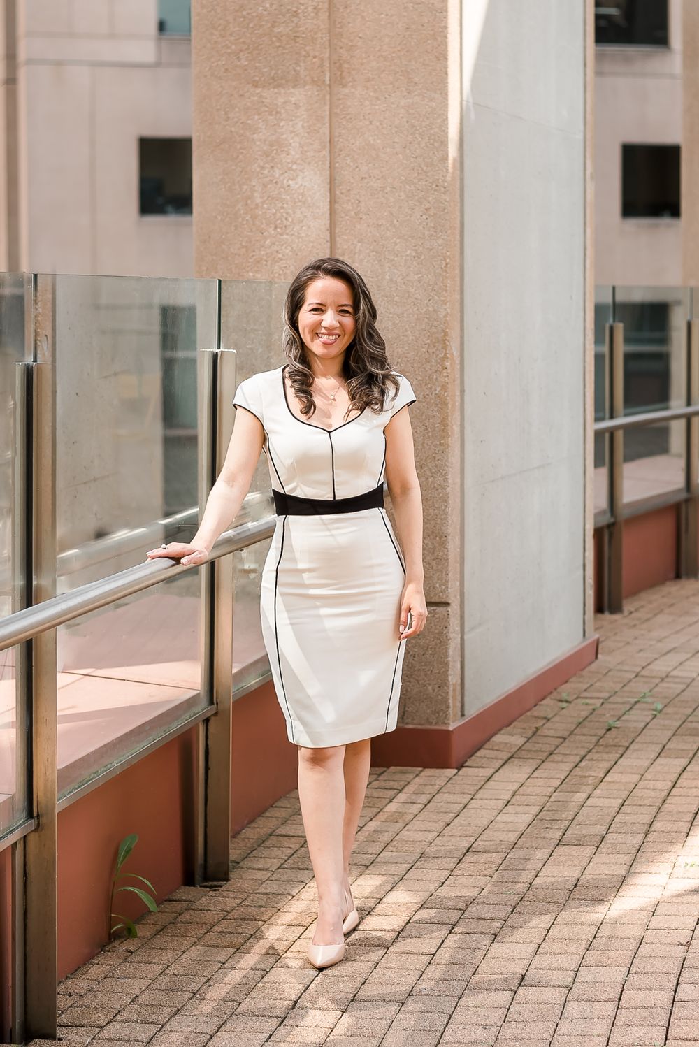 A woman stylishly dressed in a white dress stands for a branding photo session.