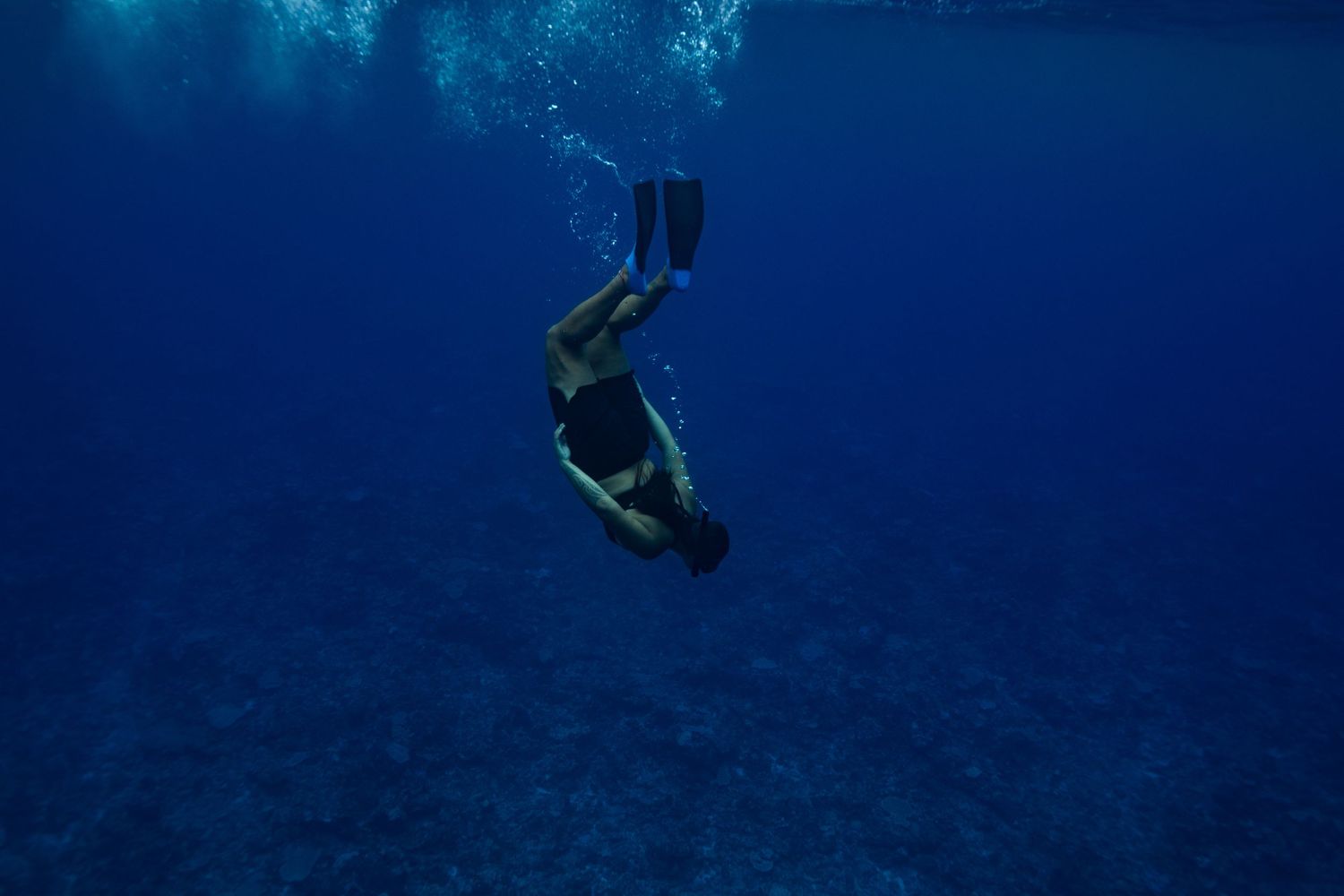 A scuba diver descends into deep blue ocean waters during an underwater dive.