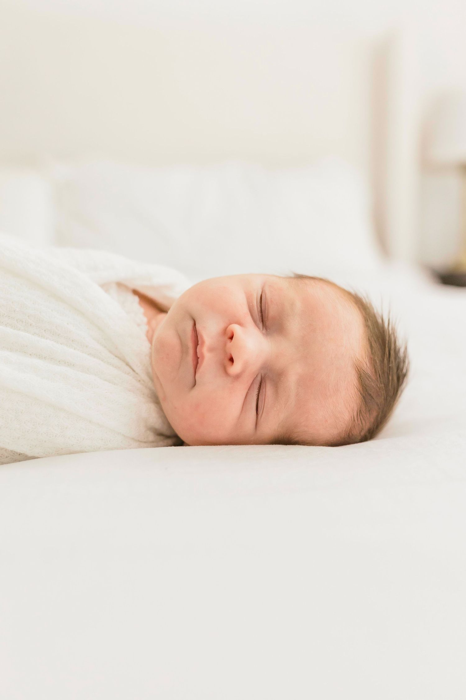 Close-up of sleeping baby's face on white bedding with natural light.