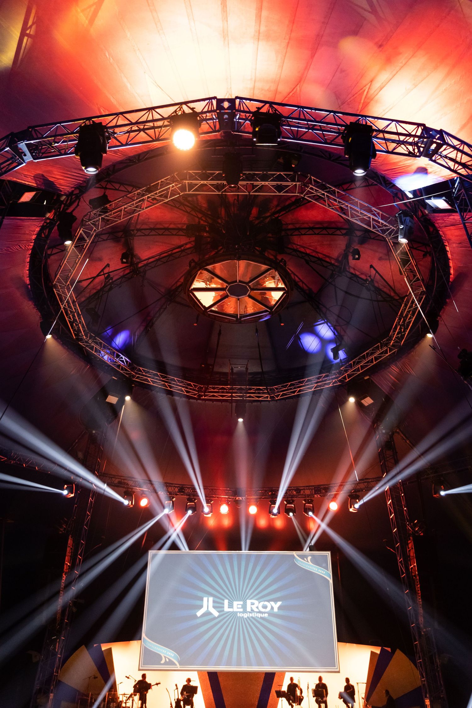 Concert venue stage with dramatic red lighting and professional truss rigging system overhead.