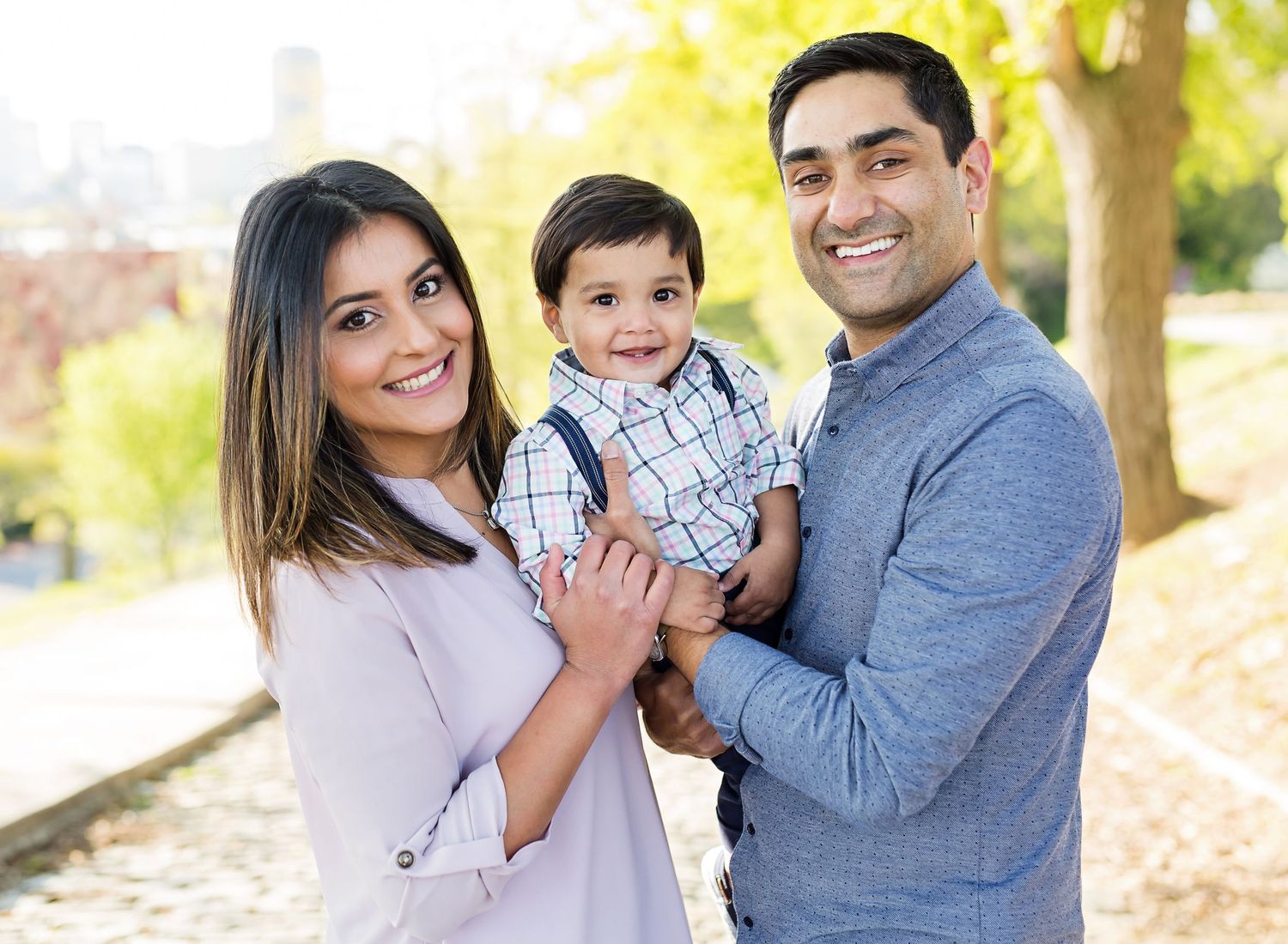 A young family poses together outdoors on a sunny autumn day wearing casual clothing.
