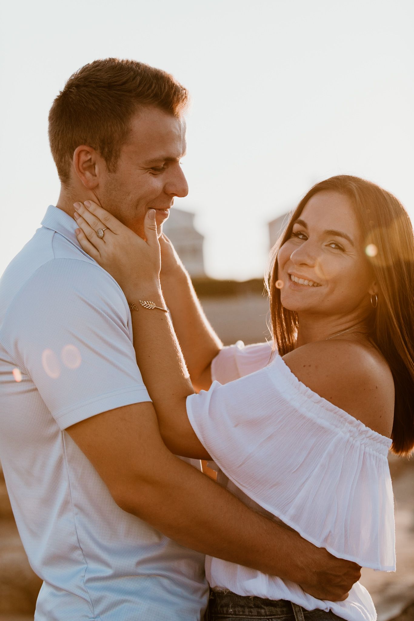 A couple shares an intimate moment in white summer outfits during golden hour.