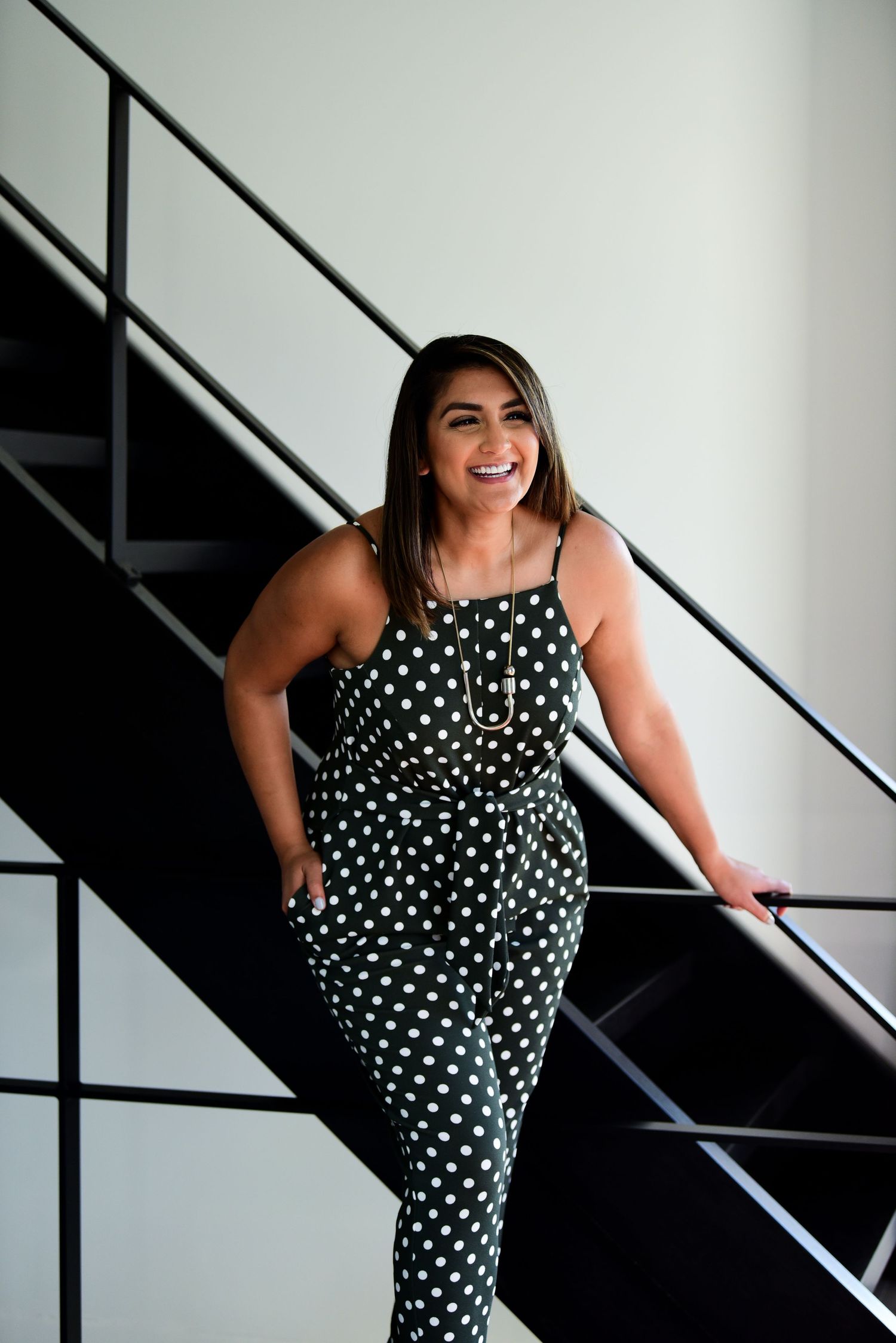 Polka dot jumpsuit fashion photo against modern staircase background.