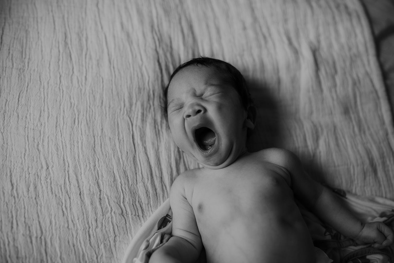 A newborn baby boy yawns sleepily during an Oahu newborn photoshoot.