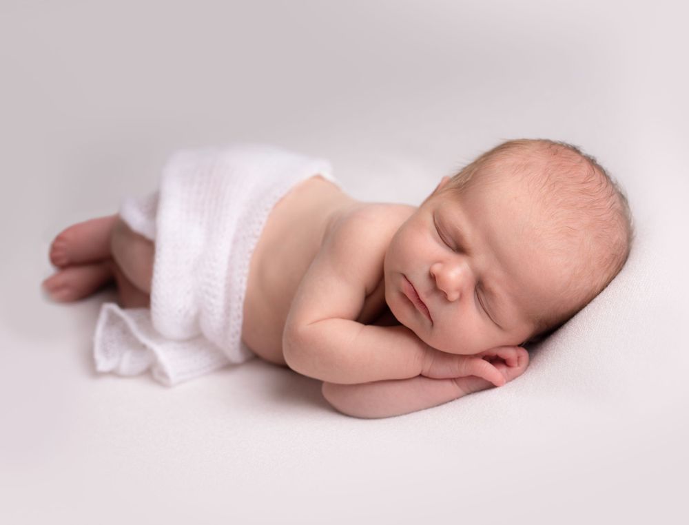 Peaceful sleeping newborn baby wrapped in white fabric against neutral background.