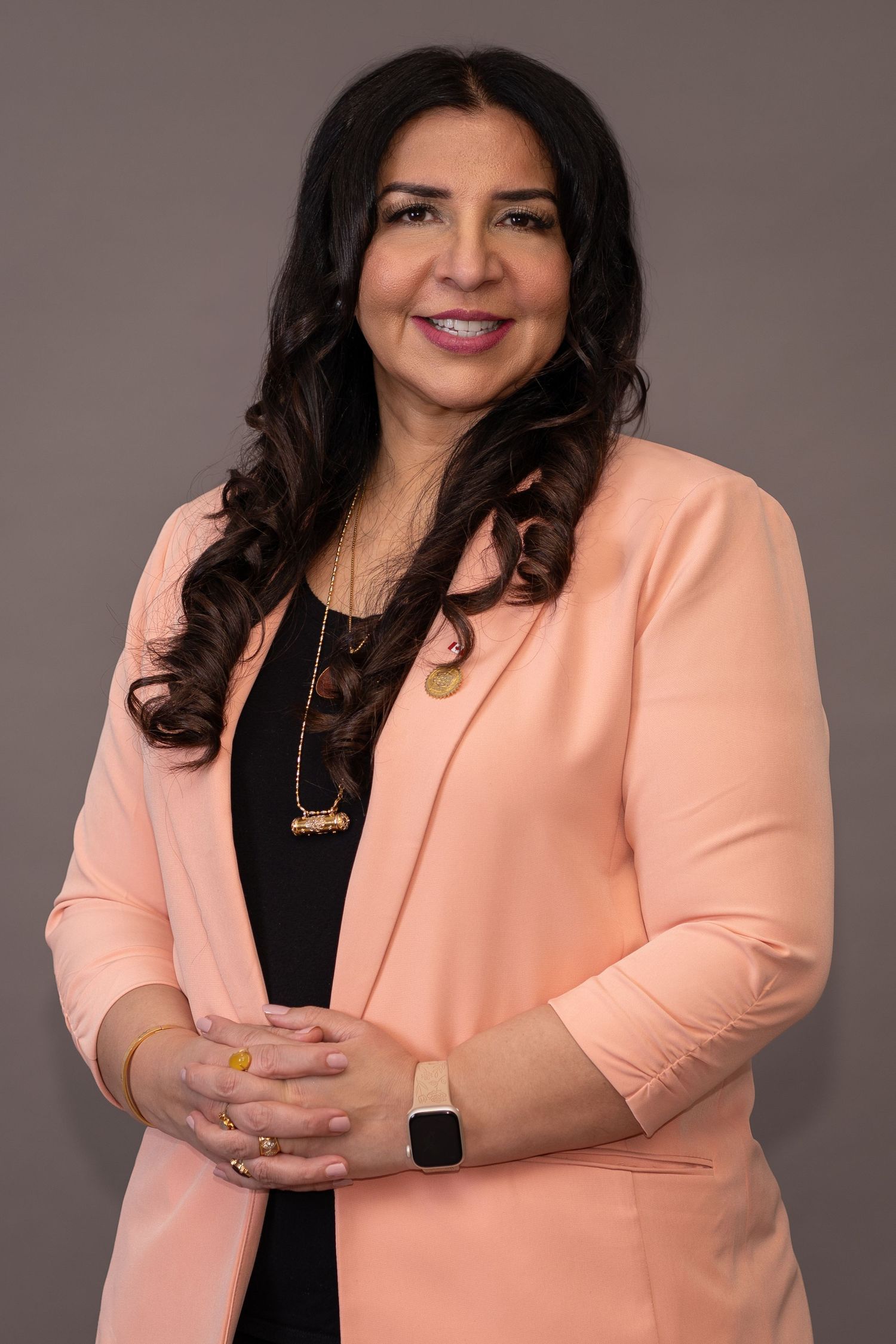 Professional headshot of woman in peach blazer against gray background.