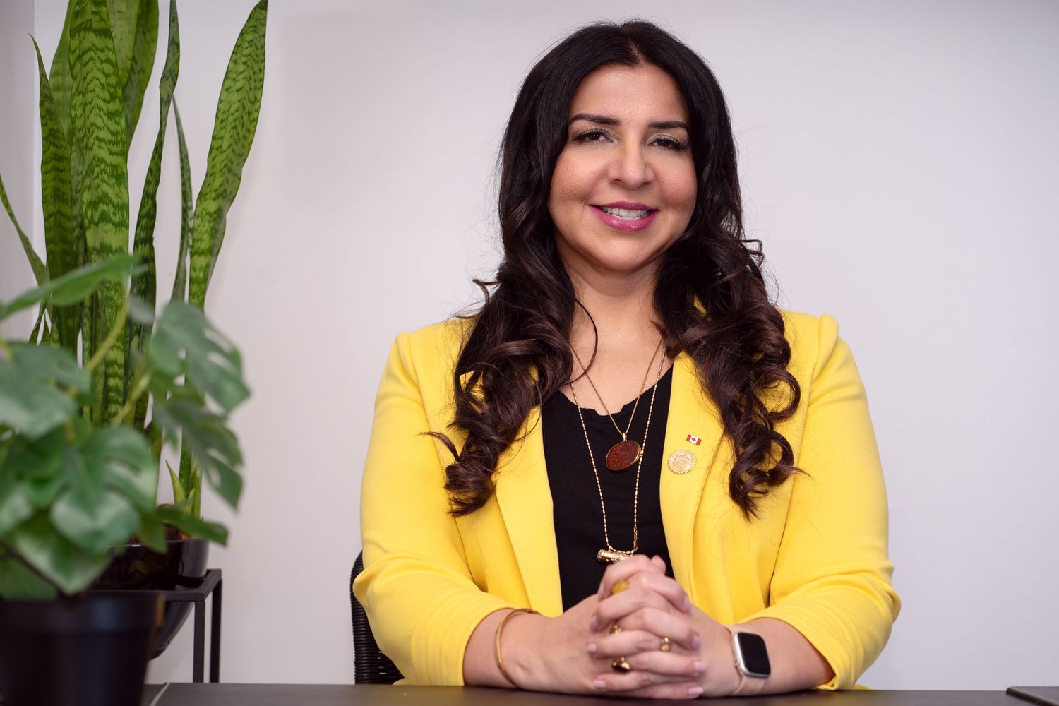 Woman in yellow blazer seated at desk with indoor plant.