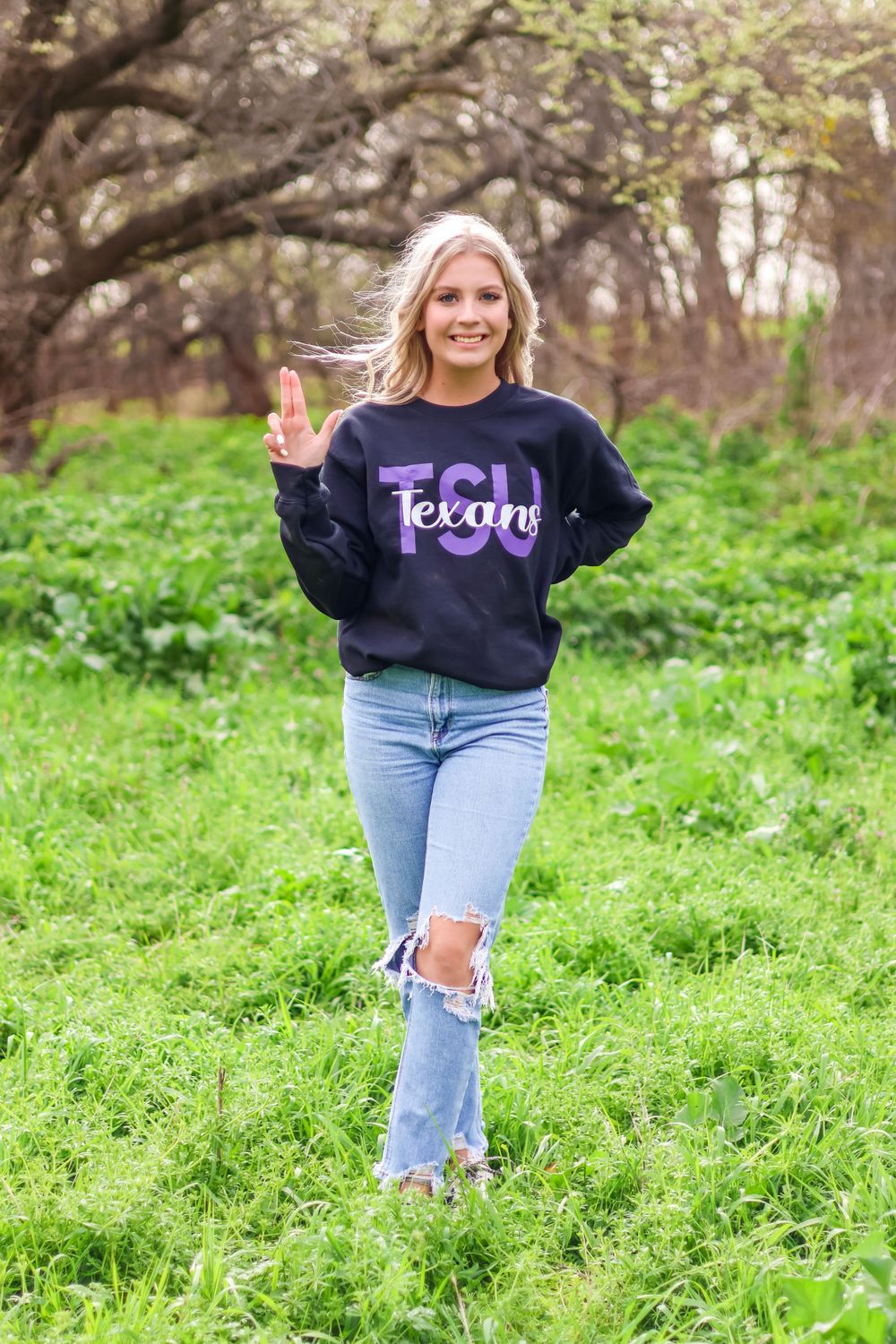 Person in college sweatshirt and ripped jeans poses in green spring field.