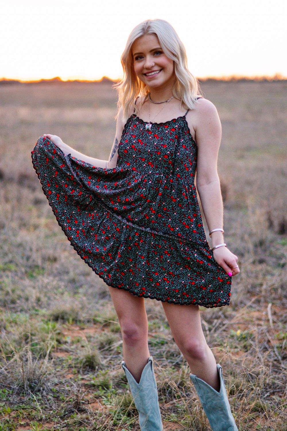 Person twirling in floral dress and turquoise boots in sunset field.