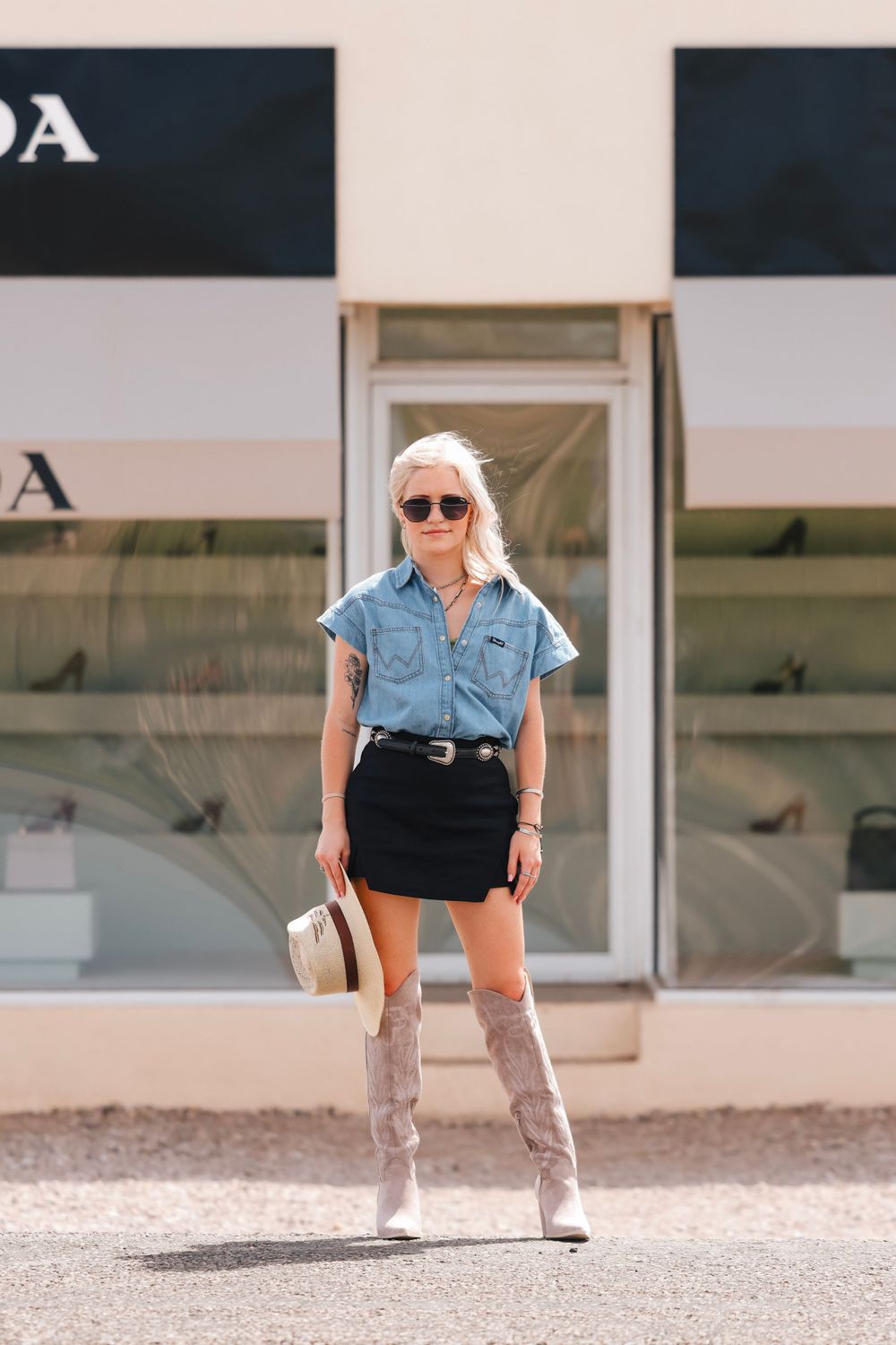 A stylish outfit featuring knee-high boots, denim shirt and mini skirt in front of a storefront.