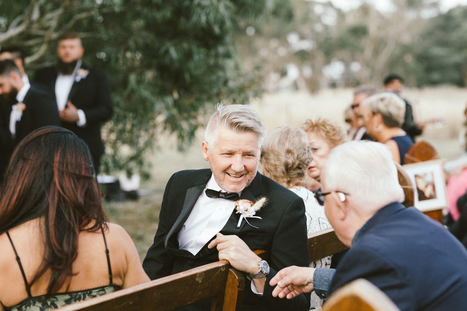 Candid moment of wedding guests laughing during outdoor ceremony.