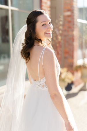 A smiling bride in a white wedding dress standing on brick steps. Holly Hotel