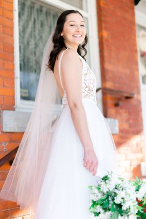 A smiling bride in a white wedding dress standing on brick steps.